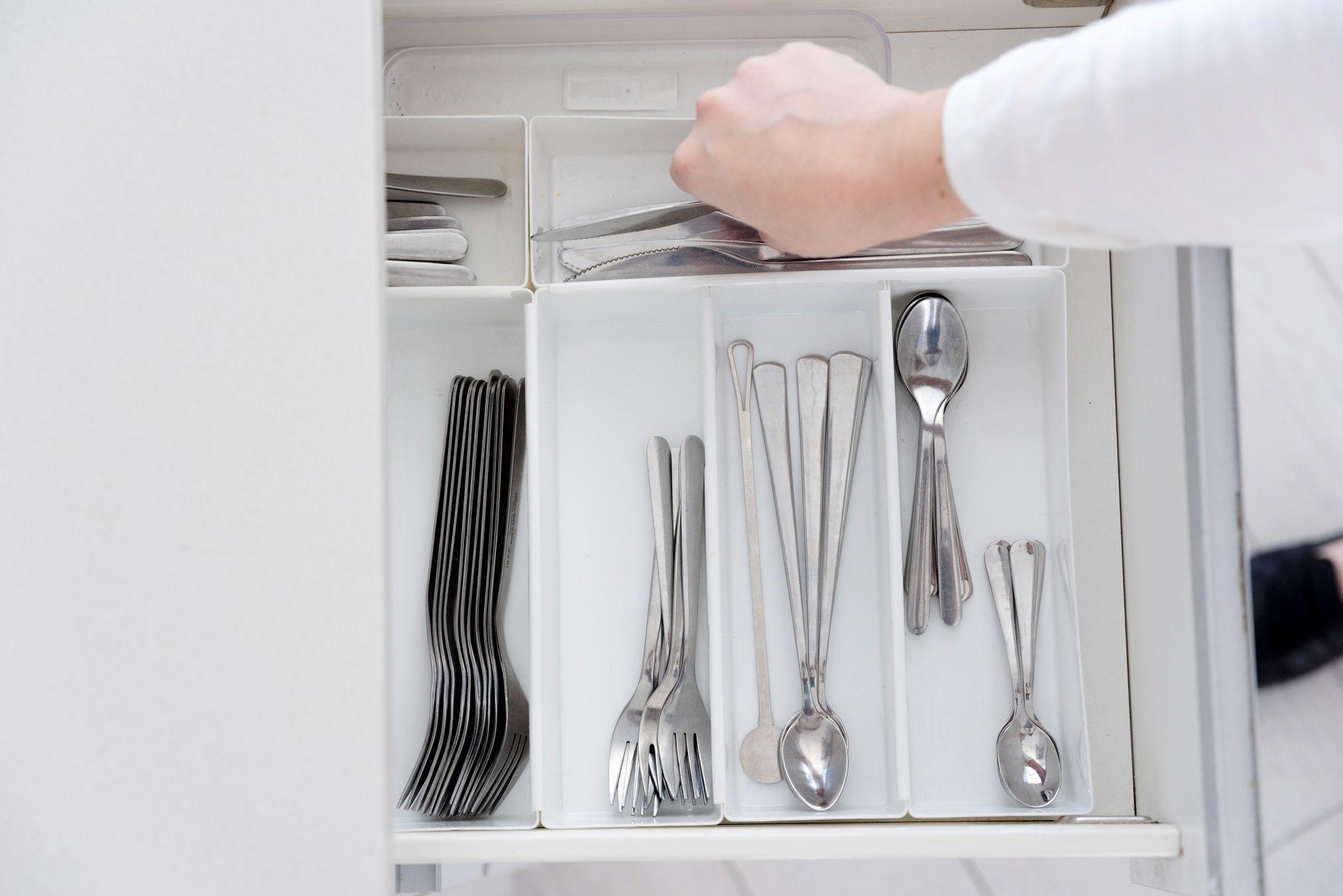 Offene Schublade mit Besteckorganizer, in dem Gabeln, Messer und Löffel ordentlich sortiert sind, eine Hand greift nach einem Messer.
